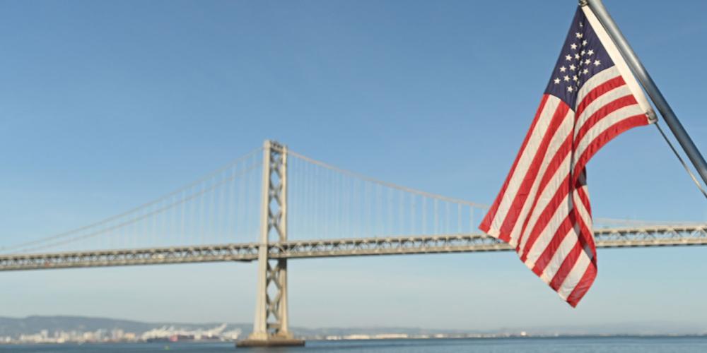An American flag in front of the San Francisco-Oakland Bay Bridge.