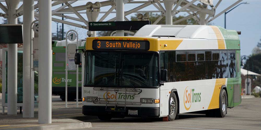 A SolTrans bus sits at a bus stop at the Vallejo Transit Center on a sunny day.